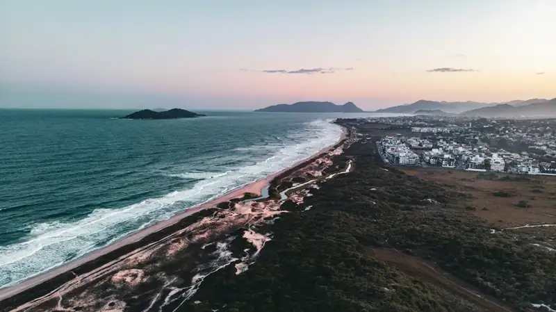 Praia longa de mar aberto com a ilha do Campeche no horizonte e o bairro ao lado