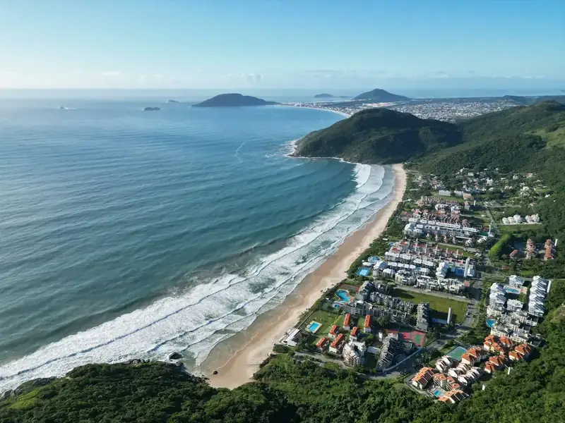 Vista aérea de praia com ondas e bairro planejado à beira-mar no norte da Ilha