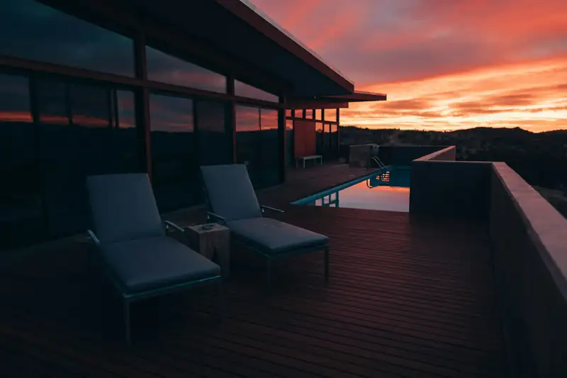 Deck de madeira de uma casa em Cacupé ao pôr do sol, com espreguiçadeiras e a Baía Norte ao fundo