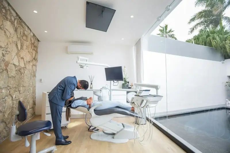 Dentista atendendo uma paciente no consultório da Brandt Odontologia, com janelas amplas e palmeiras do lado de fora