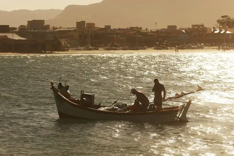 Pescadores numa canoa na baía, contra o sol do fim de tarde