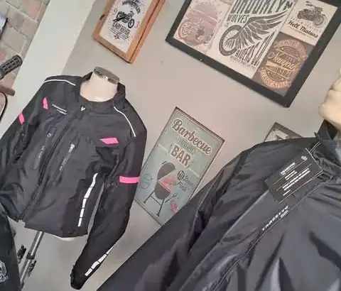 Jaquetas e calças pretas para motociclista com detalhes rosa e refletivos expostas na oficina